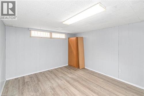 Finished room featuring wood-finish flooring, light blue vertical paneling, and an acoustic tile ceiling with fluorescent lighting - 112 Nash Road S, Hamilton, ON - Indoor