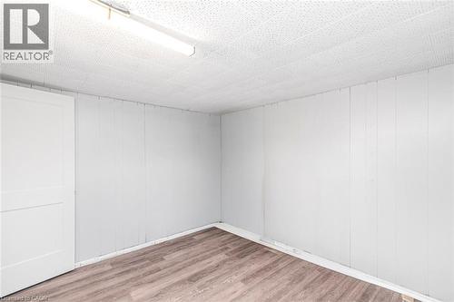 Room featuring wood-finish flooring, white paneled walls, a white ceiling with acoustic tiles, a white paneled door, and a fluorescent ceiling light fixture - 112 Nash Road S, Hamilton, ON - Indoor Photo Showing Other Room