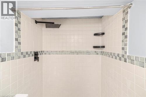Shower enclosure featuring cream-colored square tiles, a decorative mosaic tile accent band, a square matte black rainfall showerhead, and matte black corner shelving - 112 Nash Road S, Hamilton, ON - Indoor Photo Showing Bathroom