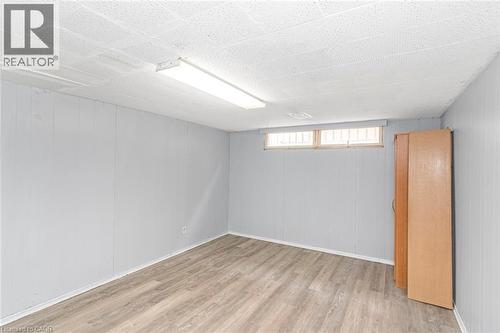 Spacious room featuring light wood-finish flooring, light grey paneled walls, and a white acoustical tile ceiling with a fluorescent light fixture - 112 Nash Road S, Hamilton, ON - Indoor