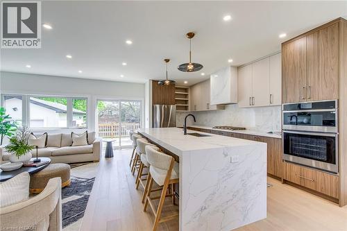 Contemporary kitchen featuring a waterfall island, integrated stainless steel appliances, two-tone cabinetry, and wood-finish flooring - 1411 Mountain Grove Avenue, Burlington, ON - Indoor Photo Showing Kitchen With Upgraded Kitchen