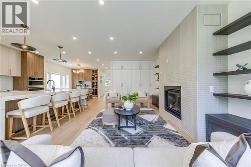 Open-concept living area featuring a modern fireplace with a tiled surround, light wood-finish flooring, recessed lighting, and a kitchen island with seating - 1411 Mountain Grove Avenue, Burlington, ON - Indoor Photo Showing Living Room With Fireplace