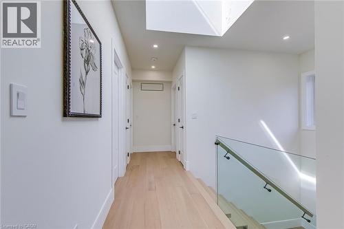 Bright hallway featuring light wood-finish flooring, recessed lighting, white trim, and a glass-paneled staircase railing - 1411 Mountain Grove Avenue, Burlington, ON - Indoor Photo Showing Other Room