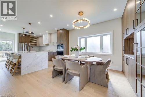 Open-concept kitchen and dining area featuring light wood-finish flooring, a white waterfall island with seating, integrated stainless steel appliances, and extensive built-in cabinetry - 1411 Mountain Grove Avenue, Burlington, ON - Indoor