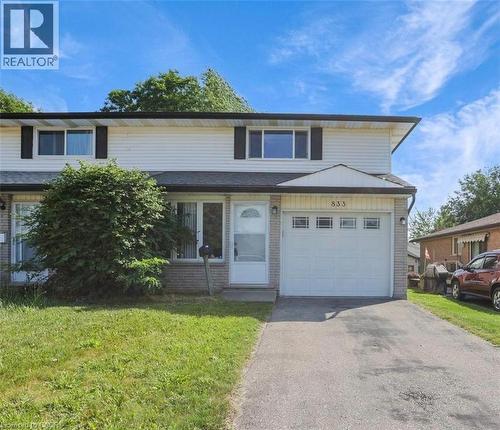 Two-story townhome featuring a neutral exterior siding, a white garage door with upper window panels, and a concrete driveway - 833 Doon Village Road, Kitchener, ON - Outdoor With Facade