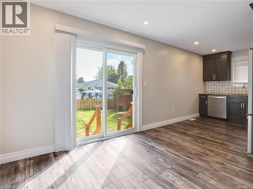 Sliding glass patio doors opening to a backyard with wood-finish flooring, recessed lighting, and a kitchen area featuring dark cabinetry, stainless steel appliances, and a mosaic tile backsplash - 833 Doon Village Road, Kitchener, ON - Indoor