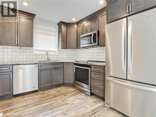 Modern kitchen featuring wood-finish flooring, grey cabinetry, stainless steel appliances, and a patterned tile backsplash - 833 Doon Village Road, Kitchener, ON - Indoor Photo Showing Kitchen With Upgraded Kitchen