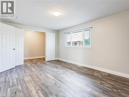 Spacious interior featuring wood-finish flooring, neutral wall tones, a ceiling-mounted light fixture, and a large window with white trim - 833 Doon Village Road, Kitchener, ON - Indoor Photo Showing Other Room