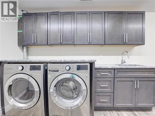 Laundry space featuring gray shaker-style cabinetry, a built-in sink with a chrome faucet, light-toned countertops, and wood-finish flooring - 833 Doon Village Road, Kitchener, ON - Indoor Photo Showing Laundry Room