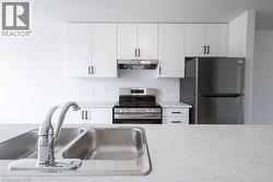Kitchen featuring white upper and lower cabinetry with black hardware, stainless steel appliances, and a dual basin sink with chrome faucet - 