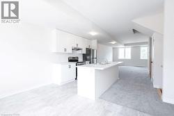 Contemporary kitchen featuring white cabinetry, stainless steel appliances, a center island with sink, and light gray tiled flooring - 