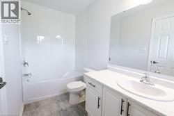 Full bathroom featuring a single vanity with an integrated sink, white cabinetry, a large mirror, a toilet, and a bathtub with a shower and subway tile surround - 