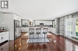 Kitchen featuring a breakfast bar area, stainless steel appliances, dark wood-style floors, white cabinets, and a kitchen island - 