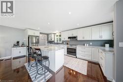 Kitchen with stainless steel appliances, white cabinetry, a center island, light stone countertops, and a breakfast bar - 