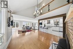 Living room featuring plenty of natural light, light wood finished floors, lofted ceiling, and suspended lighting - 