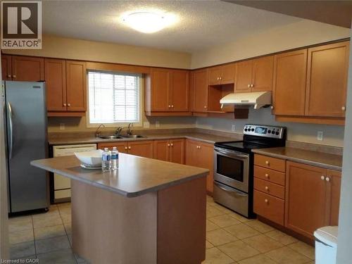 Kitchen featuring wood-finish cabinetry, stainless steel appliances, a center island with an extended countertop, a double basin sink, and tile flooring - 350 Havendale Crescent, Waterloo, ON - Indoor Photo Showing Kitchen With Double Sink