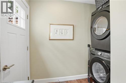 White paneled door with glass insert, stacked laundry appliances, light neutral wall color, and wood-finish flooring - 47 New Street, Hamilton, ON - Indoor Photo Showing Laundry Room