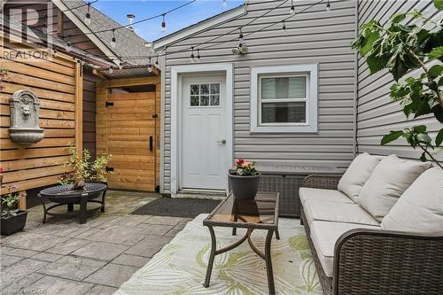 Paved patio area featuring light gray siding, horizontal wood paneling, a decorative wall-mounted fountain, and an exterior door with window panes - 47 New Street, Hamilton, ON - Outdoor With Exterior