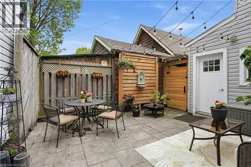 Paved outdoor patio featuring string lighting, a privacy fence, a wooden gate, and an exterior door with window panes - 47 New Street, Hamilton, ON - Outdoor With Deck Patio Veranda With Exterior