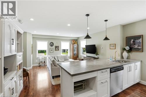 Kitchen island with integrated sink and dishwasher, featuring pendant lighting, solid surface countertop, and white cabinetry with brushed nickel hardware - 47 New Street, Hamilton, ON - Indoor