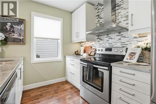 Modern kitchen featuring wood-finish flooring, white cabinetry with brushed nickel hardware, light-toned countertops, a stainless steel range, and a mosaic tile backsplash - 47 New Street, Hamilton, ON - Indoor Photo Showing Kitchen With Stainless Steel Kitchen With Double Sink With Upgraded Kitchen