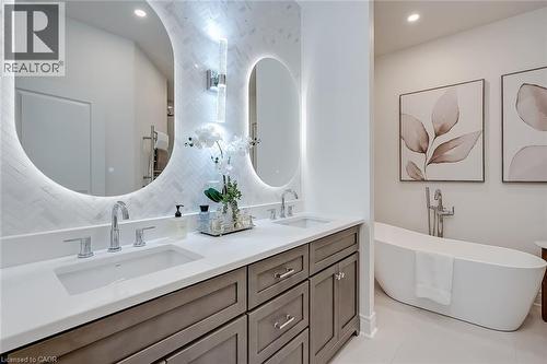 Dual illuminated oval mirrors above a spacious double vanity with a light-colored countertop and stained wood cabinetry - 4285 Couples Crescent, Burlington, ON - Indoor Photo Showing Bathroom