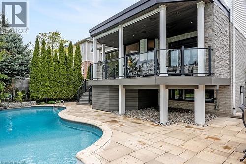 Exterior featuring a freeform swimming pool, stone patio, and an elevated covered deck with glass railings - 4285 Couples Crescent, Burlington, ON - Outdoor With In Ground Pool With Deck Patio Veranda