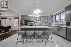 Modern kitchen featuring a large central island with a light-toned countertop, glossy gray cabinetry, and stainless steel appliances - 