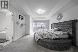 Spacious bedroom featuring light gray carpeting, tray ceiling, and a bright window with horizontal blinds - 