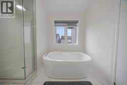 Freestanding soaking tub with chrome hardware, framed window, tile flooring, glass-enclosed shower with tiled walls and floor, and recessed lighting - 