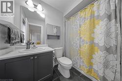 Contemporary bathroom featuring a dark gray vanity with a white countertop and integrated sink, a large wall-mounted mirror, modern three-light fixture, and dark tile flooring - 