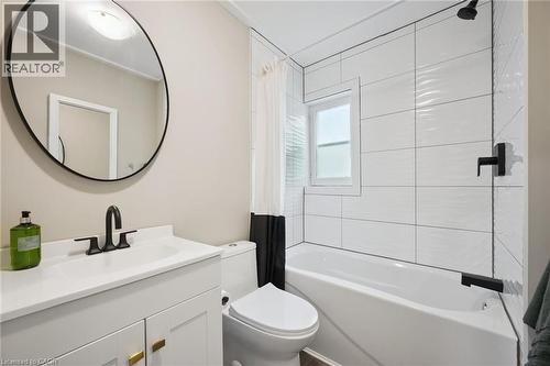 Bathroom featuring a white vanity with gold-tone hardware, a circular mirror, and matte black plumbing fixtures - 15 Gordon Avenue, Kitchener, ON - Indoor Photo Showing Bathroom