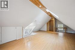 Spacious attic area featuring wood-finish flooring, a white spindle railing, and a window for natural light - 
