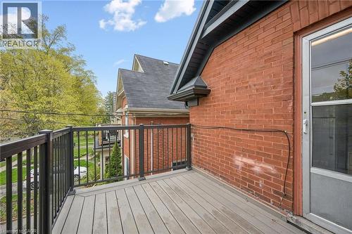 Outdoor deck featuring composite decking, black metal railings, and a red brick exterior wall with a storm door - 15 Gordon Avenue, Kitchener, ON - Outdoor With Exterior