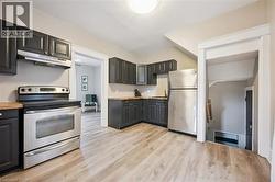 Kitchen featuring dark cabinetry, stainless steel appliances, wood-finish countertops, and light wood-finish flooring - 