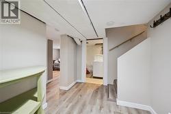 Finished lower level with wood-finish flooring, light-toned walls, recessed lighting, and a partial staircase featuring a wood handrail - 