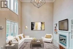 Vaulted ceiling living area featuring a geometric chandelier, abundant natural light from large windows, a fireplace with integrated shelving, and soft carpet flooring - 