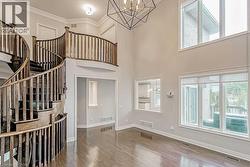 Two-story living area featuring a grand spiral staircase with wood railing, large windows, wood-finish flooring, and a contemporary chandelier - 