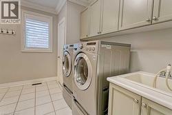 Dedicated laundry area featuring a utility sink with a pull-out sprayer, light-toned cabinetry, and tile flooring - 