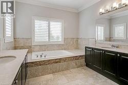 Spacious bathroom featuring a built-in tub, dual vanities with integrated sinks, and plantation shutters on multiple windows - 