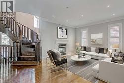 Hardwood flooring throughout the entry and living area, featuring a grand curved staircase with wood balusters and railings, a built-in fireplace with a white mantel, recessed lighting, and crown mold - 