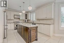 Bright kitchen featuring a central island with a light countertop, white cabinetry with dark hardware, stainless steel appliances, a tiled backsplash, and white tile flooring - 