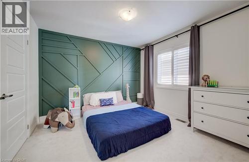 Bedroom featuring a decorative accent wall with geometric paneling, light-colored carpeting, and a window with white louvered shutters - 19 Shoreacres Drive, Kitchener, ON - Indoor Photo Showing Bedroom