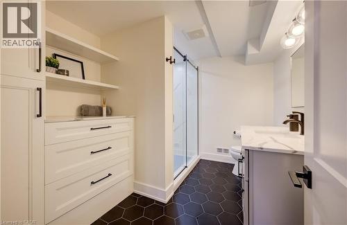 Bathroom featuring a frameless glass shower enclosure, dark hexagonal floor tiles, a vanity with a white countertop, and built-in white cabinetry with open shelving and drawers - 19 Shoreacres Drive, Kitchener, ON - Indoor