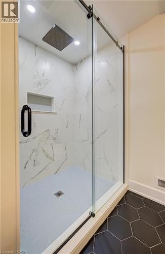 Enclosed shower featuring a sliding glass door with black hardware, white marble-look tile surround, a built-in shower niche, and an overhead rainfall showerhead - 19 Shoreacres Drive, Kitchener, ON - Indoor