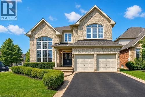 Brick exterior featuring a two-car attached garage, prominent arched and rectangular windows, a covered entry, and a manicured lawn with structured hedges - 4267 Sarazen Drive, Burlington, ON - Outdoor With Facade