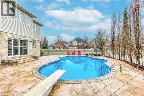 The property features a curved swimming pool with an integrated diving board, surrounded by a stamped concrete patio - 4267 Sarazen Drive, Burlington, ON - Outdoor With In Ground Pool With Deck Patio Veranda