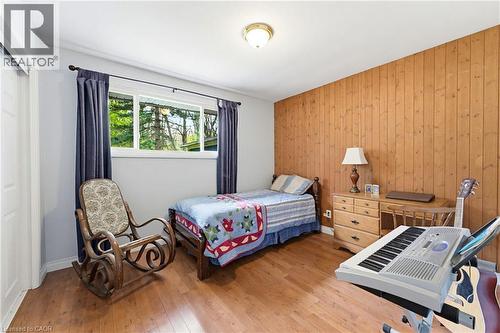 Bedroom featuring wood-finish flooring, a paneled accent wall, light gray painted walls, a flush-mount ceiling light, and a window with exterior views - 10 Huisman Lane, Hamilton, ON - Indoor Photo Showing Bedroom