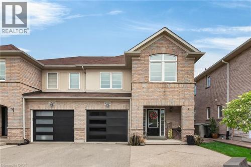Stone and stucco facade featuring a prominent gable, arched window, two distinct garage doors with horizontal glass panels, and a covered entry - 4236 Prudham Avenue, Burlington, ON - Outdoor With Facade