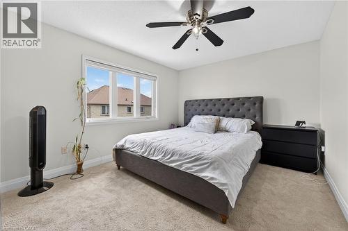 Bright room featuring light-colored carpet flooring, a multi-pane window with white trim, and a ceiling fan with dark blades - 4236 Prudham Avenue, Burlington, ON - Indoor Photo Showing Bedroom
